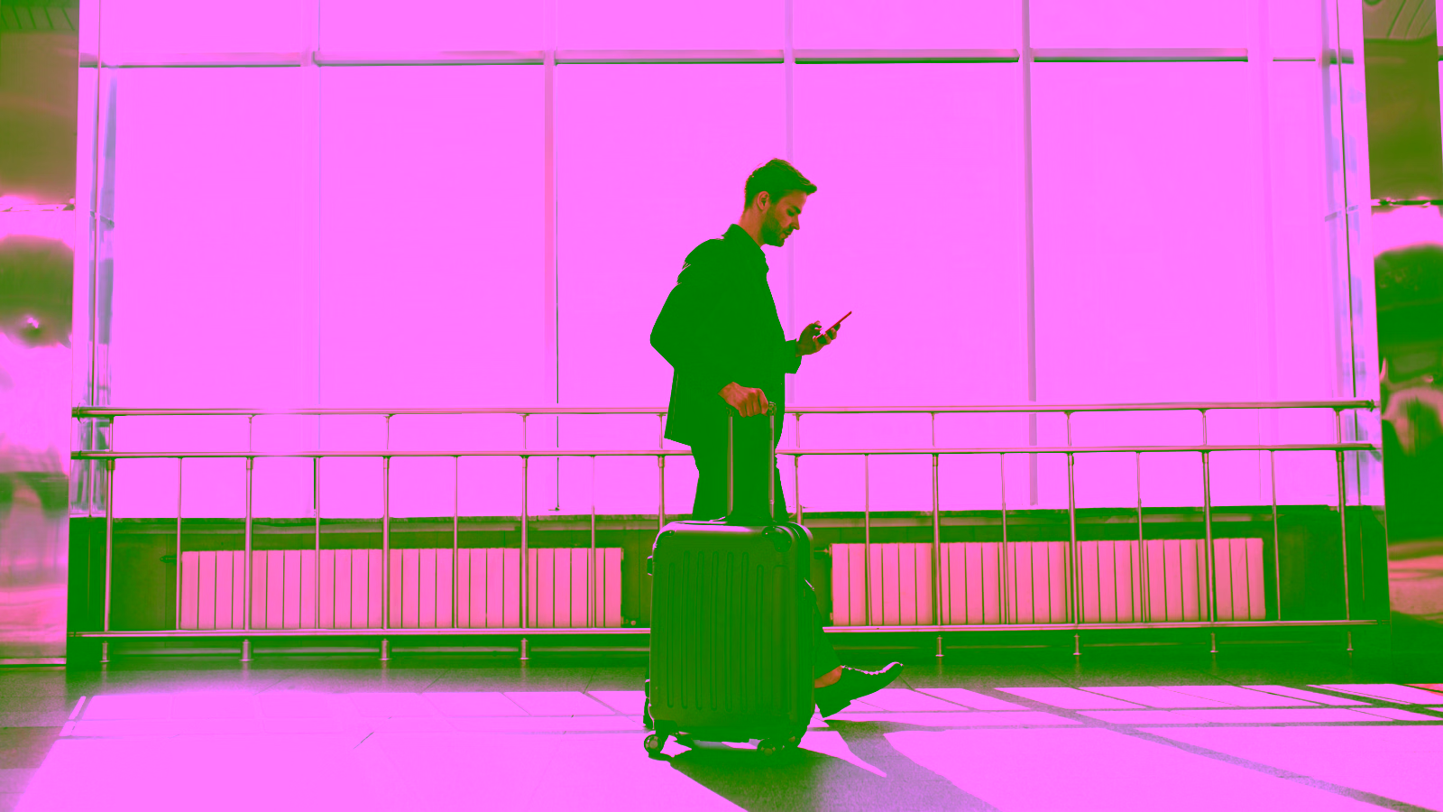 Business traveler walking through airport with suitcase while checking phone.