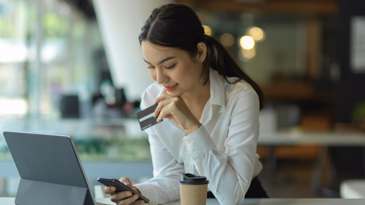 Woman reviewing credit card while using laptop and phone