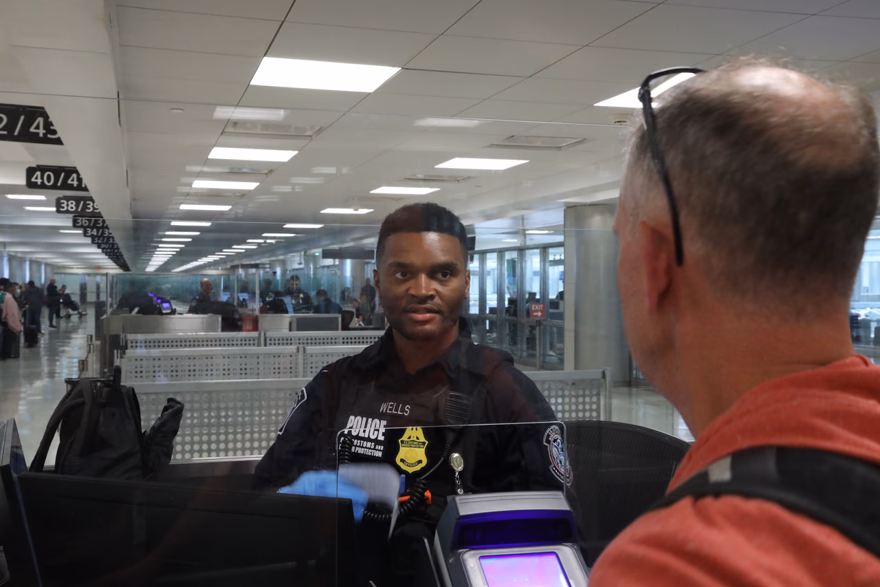 A U.S. Customs and Border Protection officer looks across his booth at an arriving traveler at Dulles International Airport